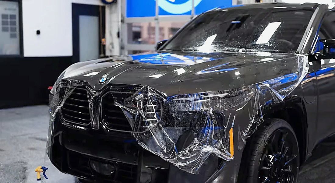 Paint protection film being installed on the front of a dark BMW SUV